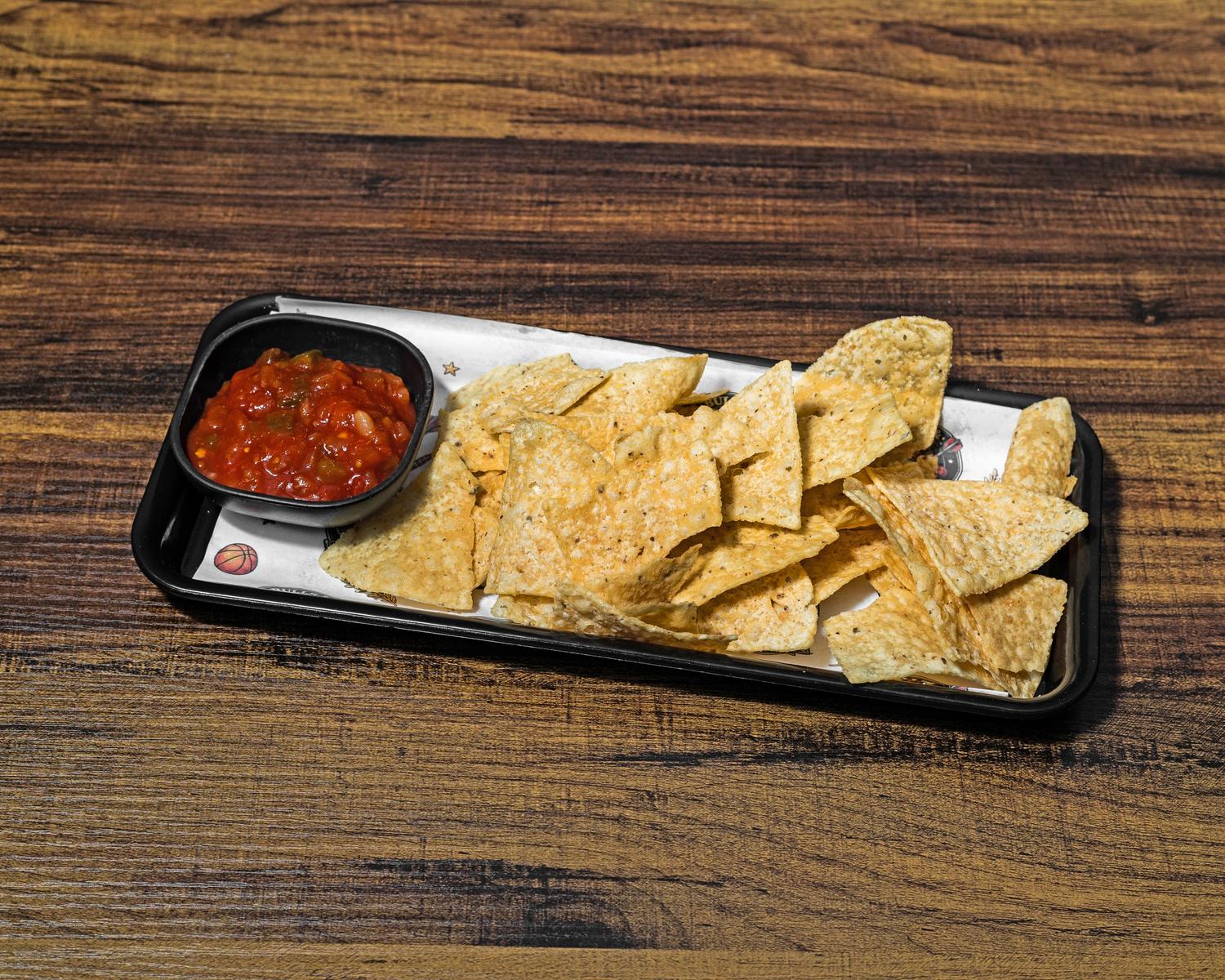Tortilla chips with a cup of chunky house salsa on a black tray
