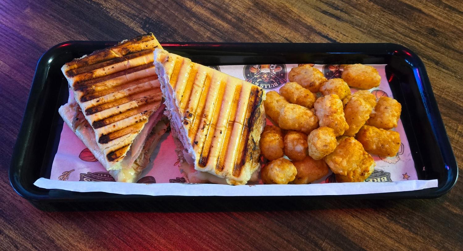 Pressed Cuban sandwich cut in half and served with tater tots