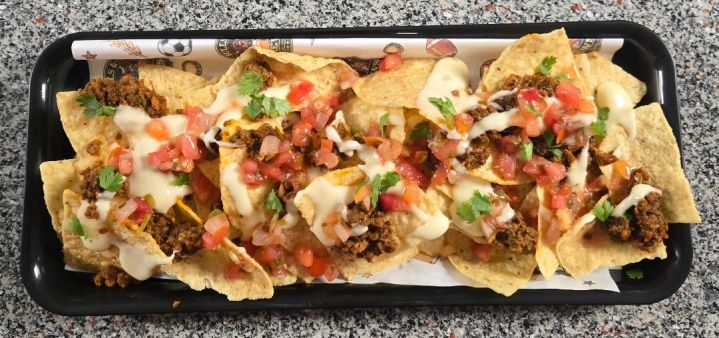 Tray of loaded nachos with seasoned beef, queso and diced tomatoes