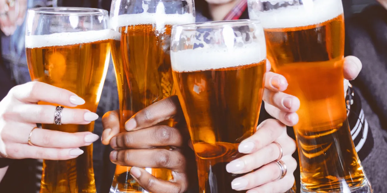 Close-up of four beer glasses clinking together