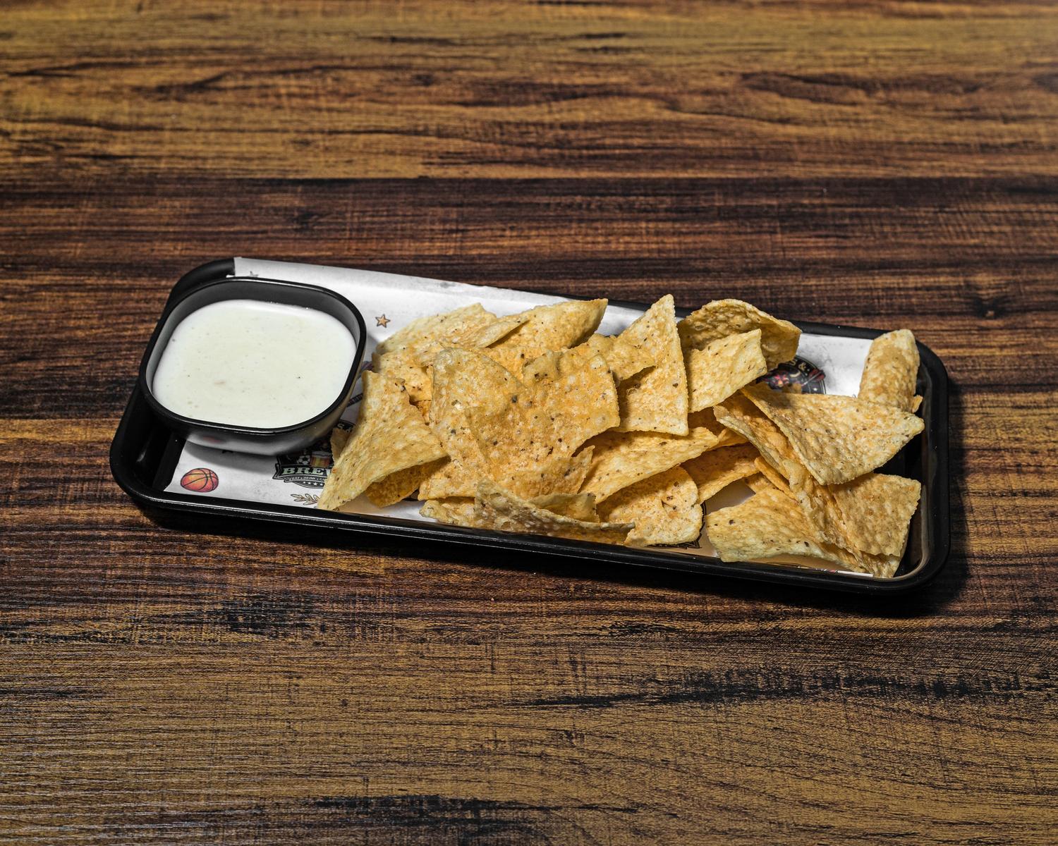Tortilla chips served with a side of warm white queso on a black tray